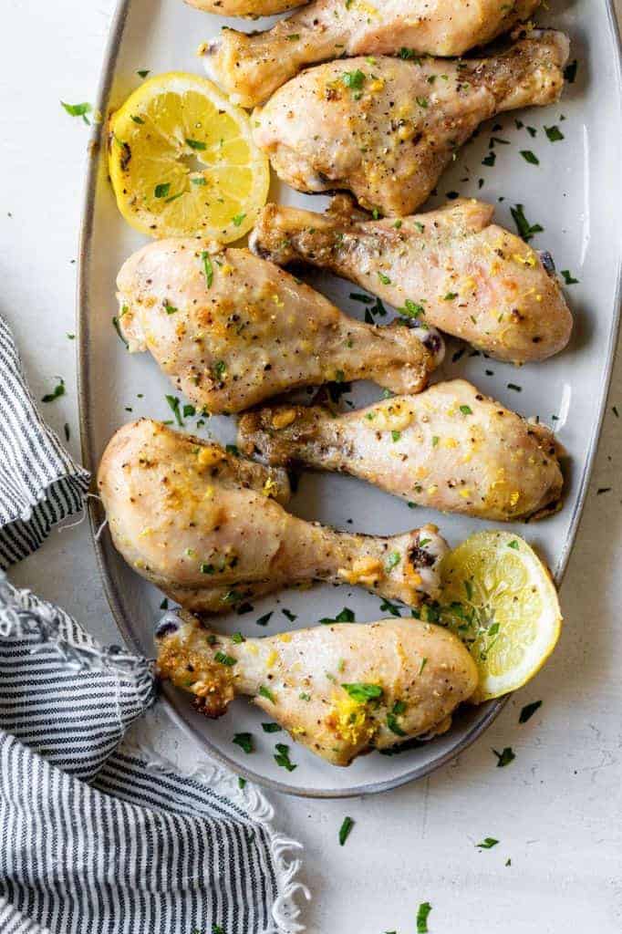 baked chicken drumsticks on a serving plate with a wedge of lemon