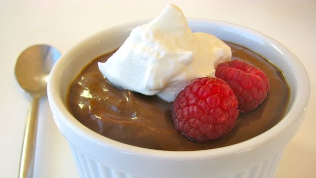 creamy avocado chocolate mouse in a ramekin topped with raspberries and cream