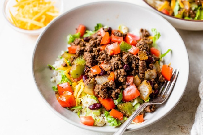 Assembling a taco bowl with ground meat and tomatoes.