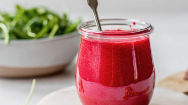 beet dressing in a glass jar with a bowl of greens