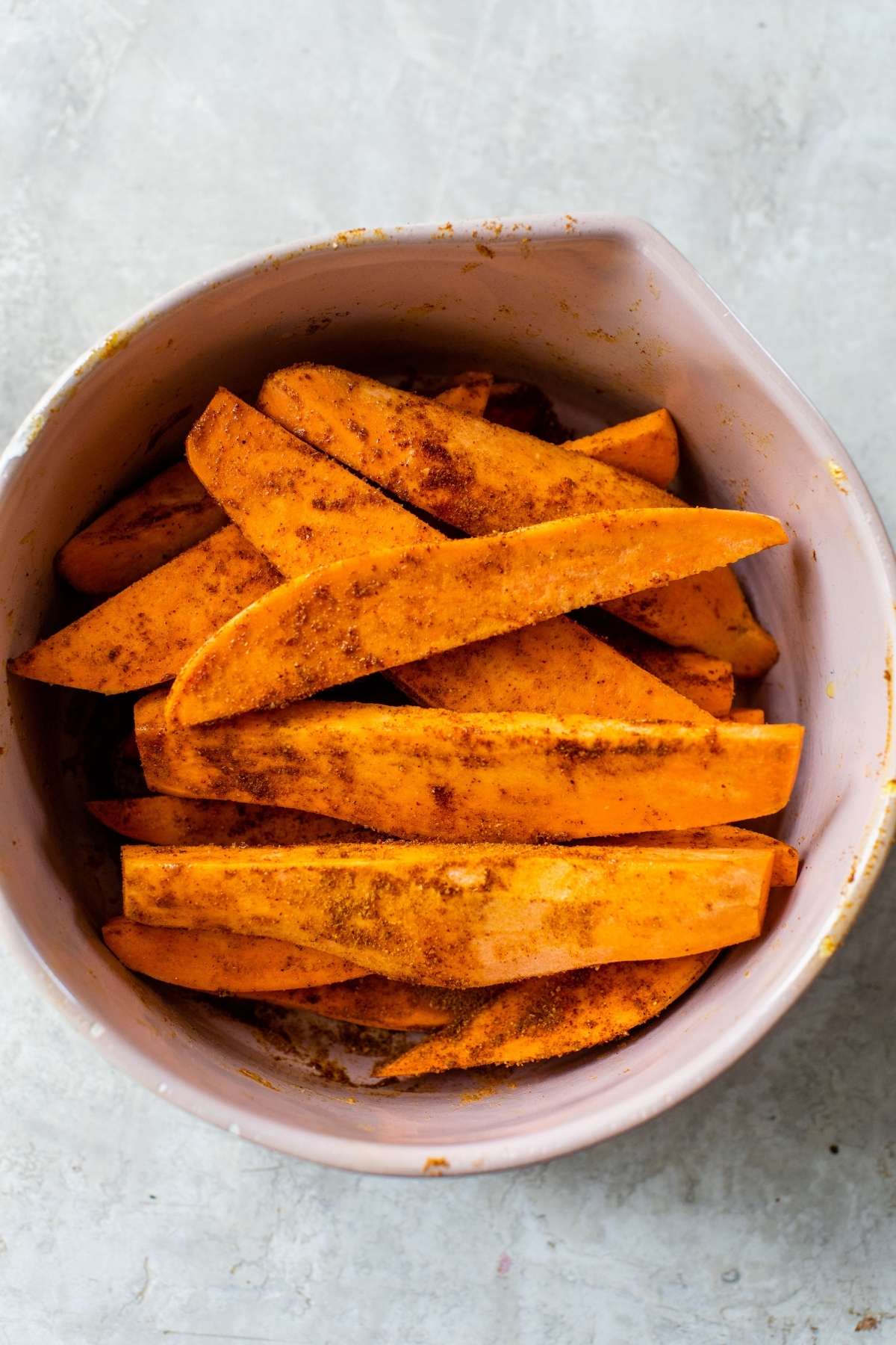 Tossing sweet potato wedges in spices.