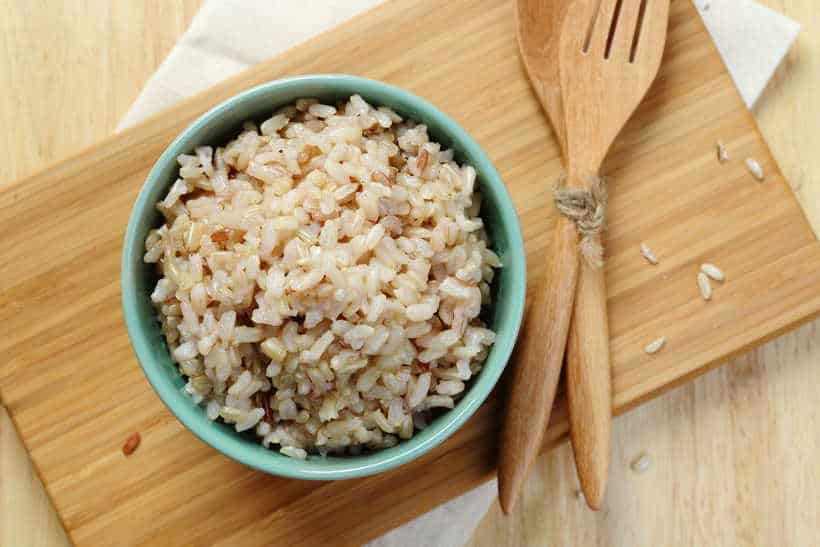 a sea foam green bowl is full of brown rice next to a set of wooden utensils