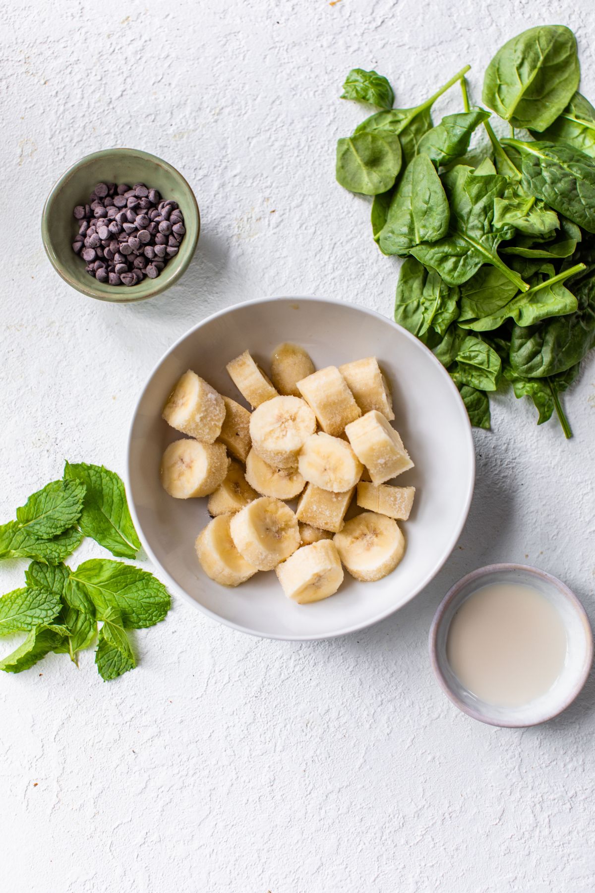 Ingredients needed to make mint chocolate chip banana nice cream divided into bowls.