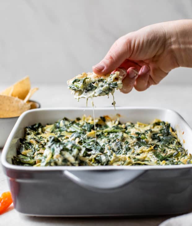 woman's hand dipping out artichoke dip