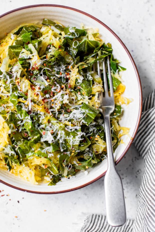 collard greens and spaghetti squash in white bowl served with a fork and topped with parmesan cheese 