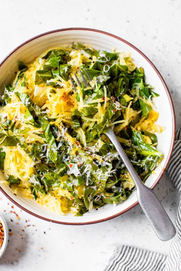 white bowl filled with Spaghetti Squash With Garlicky Collard Greens And Parmesan Cheese and served with a fork