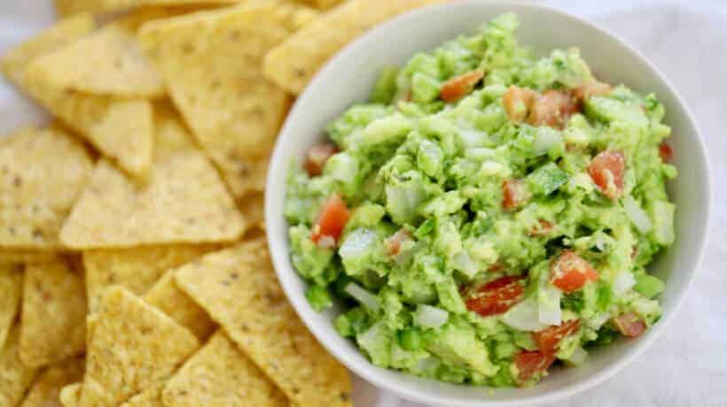 fresh guacamole in a white bowl served with corn chips