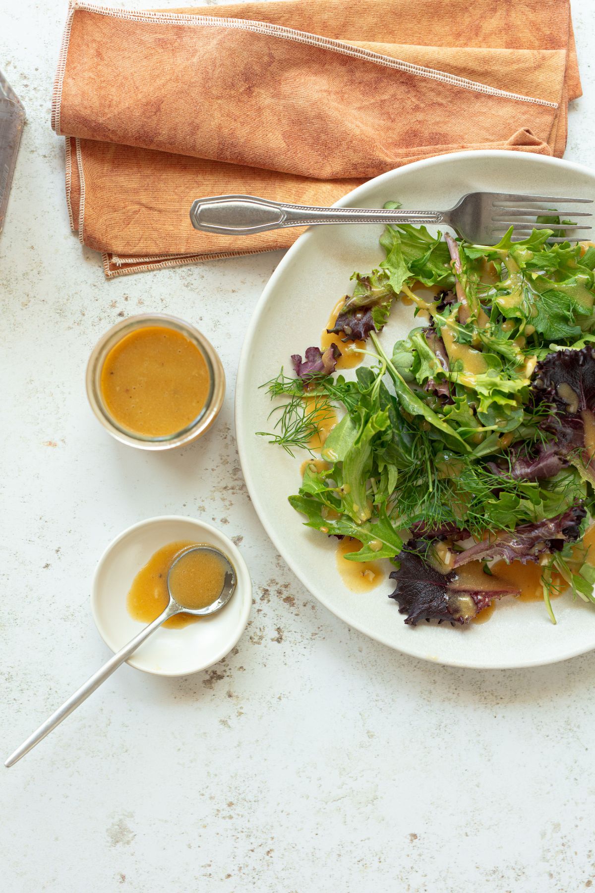 Adding dressing to a fresh green salad on a plate.