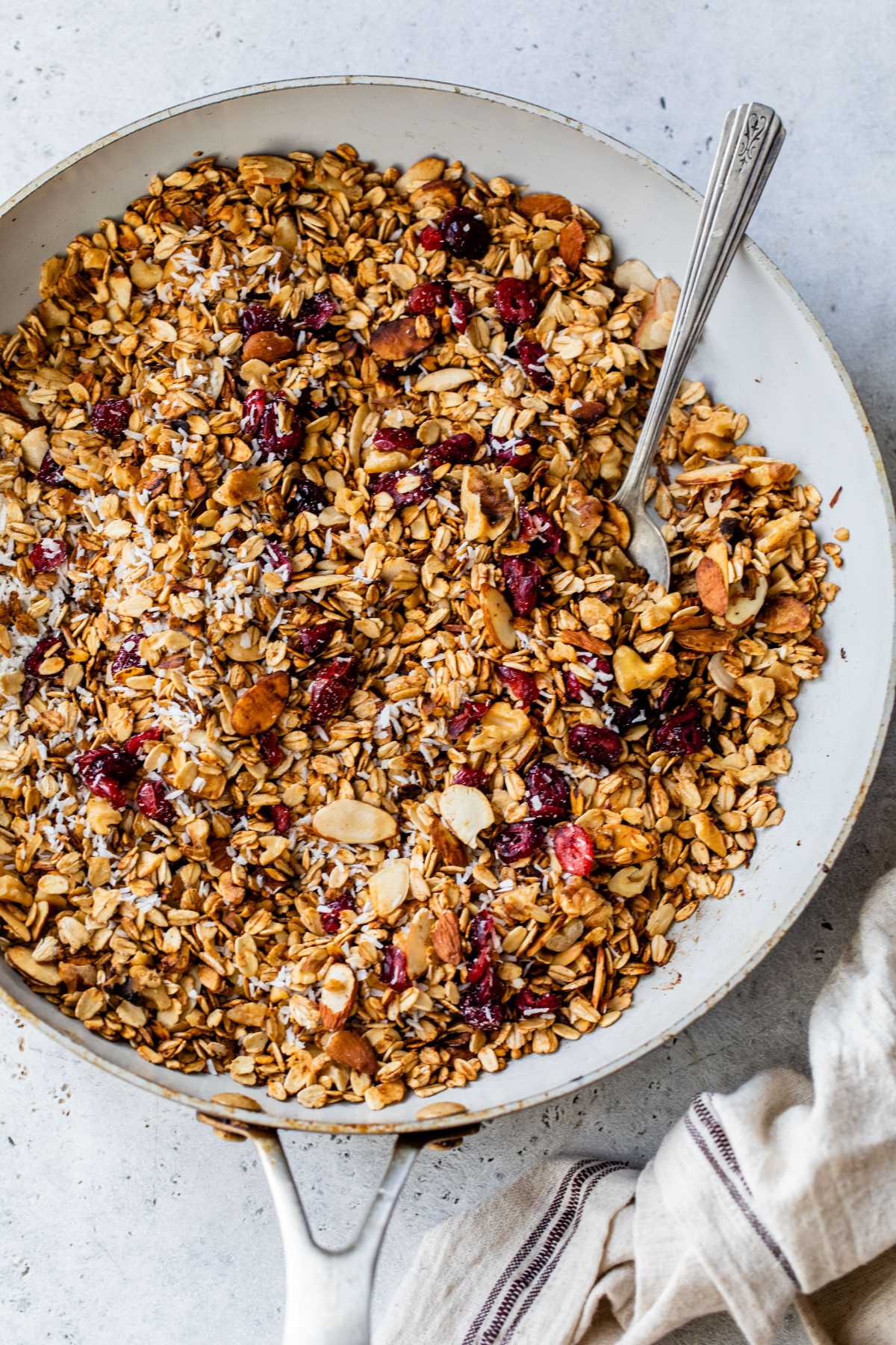 Stirring coconut and cranberries into granola in a pan.
