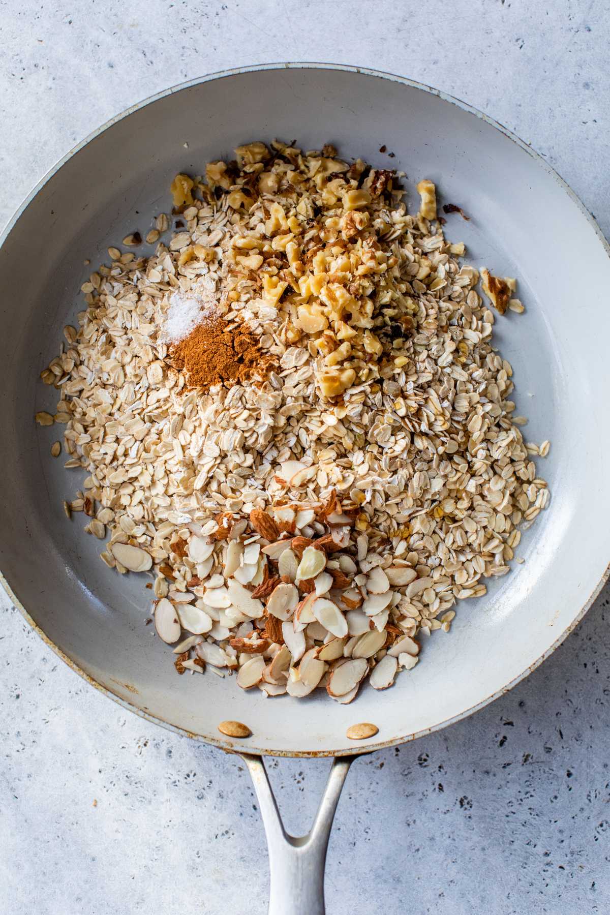 Sliced almonds, rolled oats, cinnamon, salt and walnuts added to a skillet.