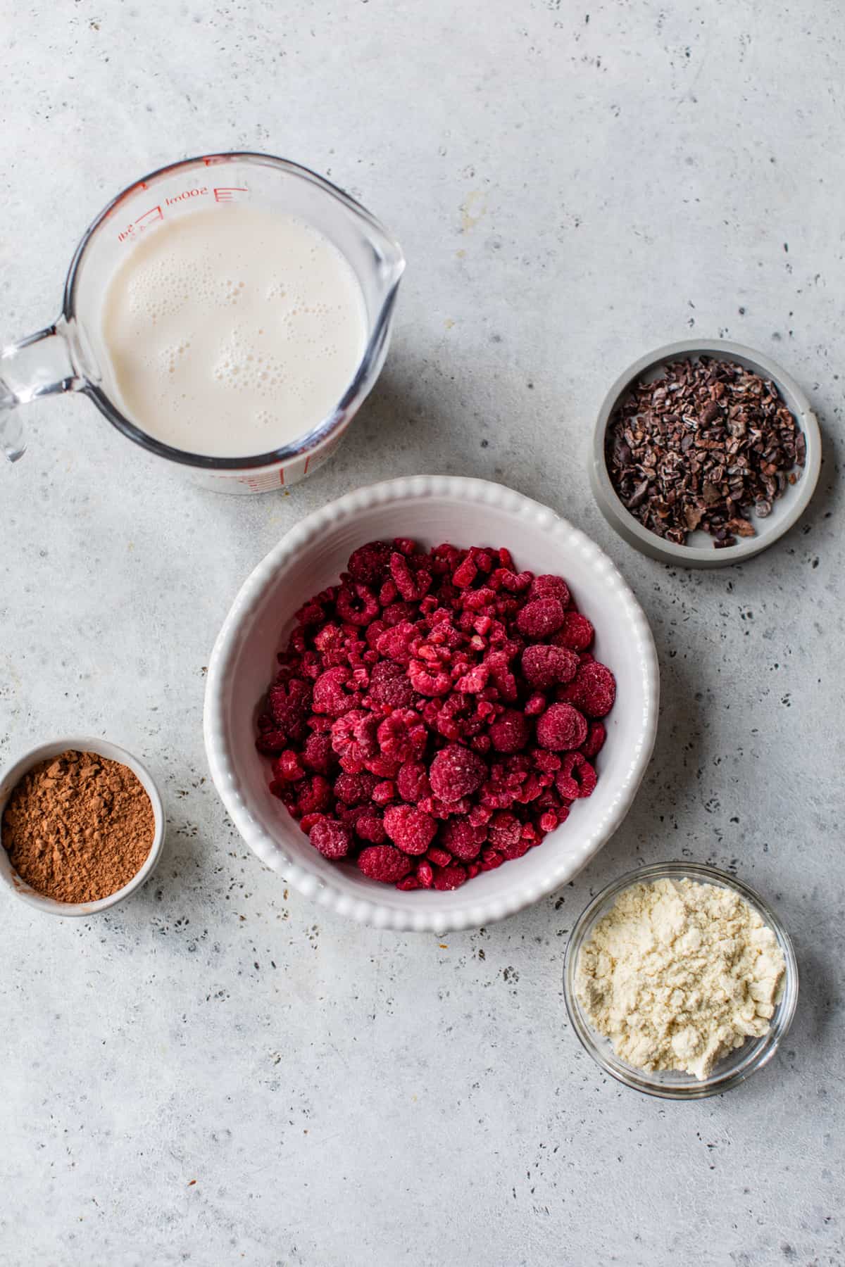 raspberries, protein powder, almond milk, cacao powder and cacao nibs measured int small bowls