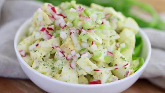 egg salad in a white bowl topped with diced radish and celery