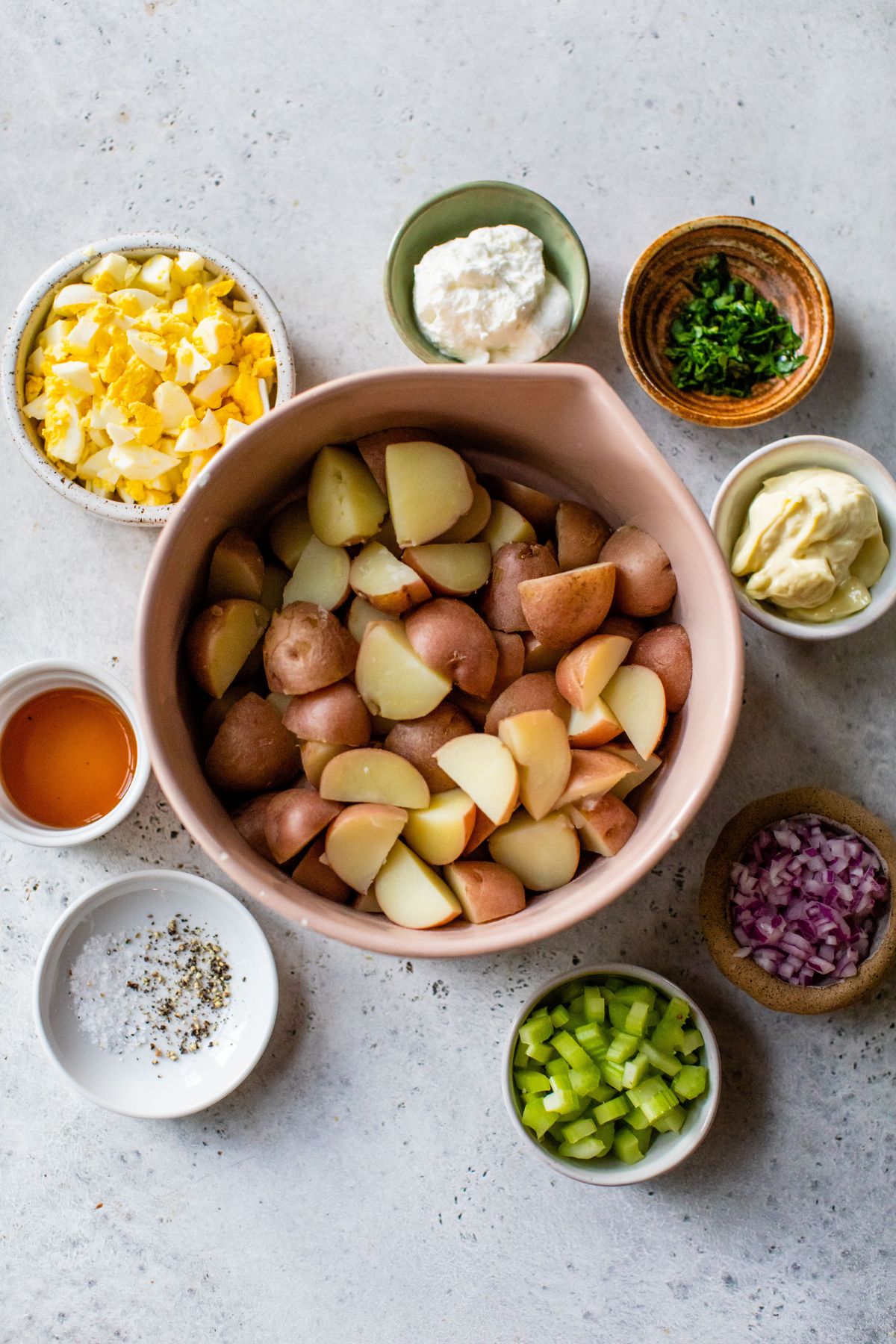 Ingredients for potato salad divided into small bowls.