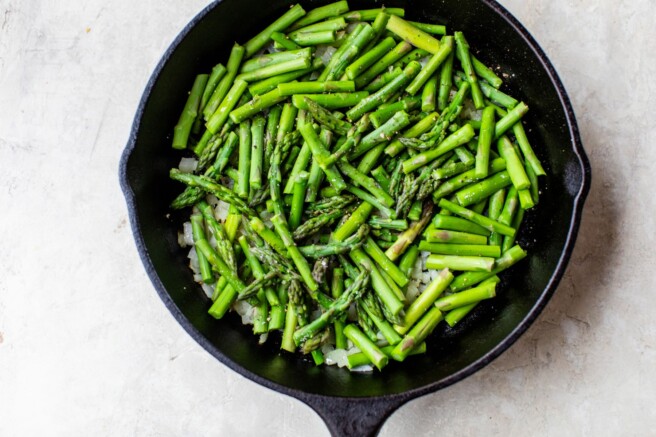 Adding asparagus to skillet with onion.