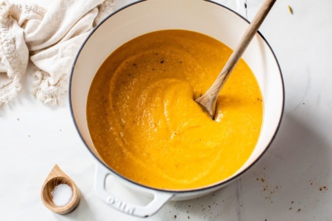 butternut squash apple soup in a large pot with a wooden spoon