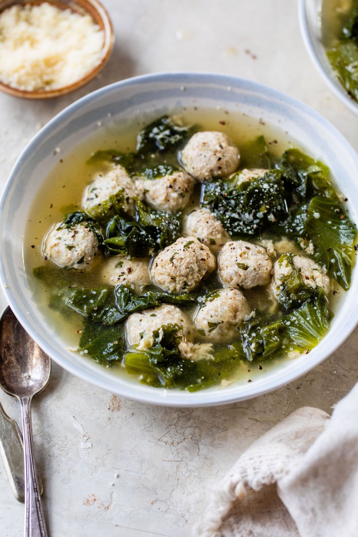 Italian wedding soup in a white bowl served with Parmesan cheese.