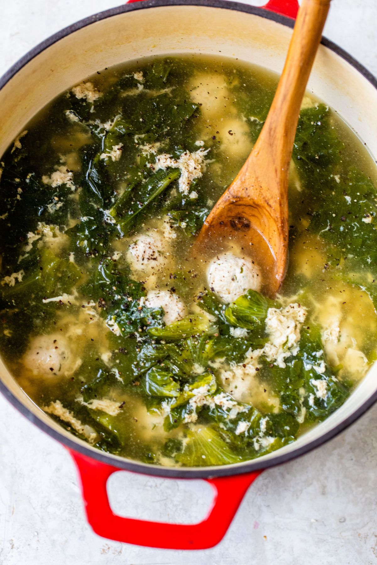 Using a wooden spoon to stir meatball soup in a large pot.