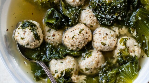 Italian wedding soup in a white bowl with a spoon.