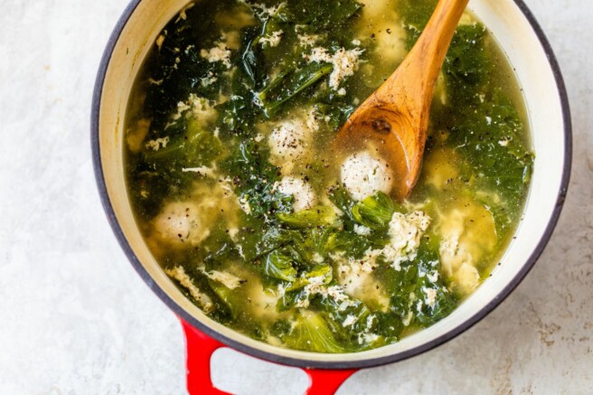 Soup made with meatballs and greens in a large pot.