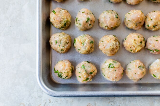 Rolled meatballs on a cookie sheet.