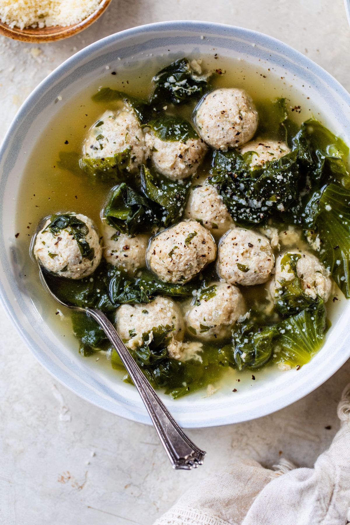 Italian wedding soup in a white bowl with a spoon.
