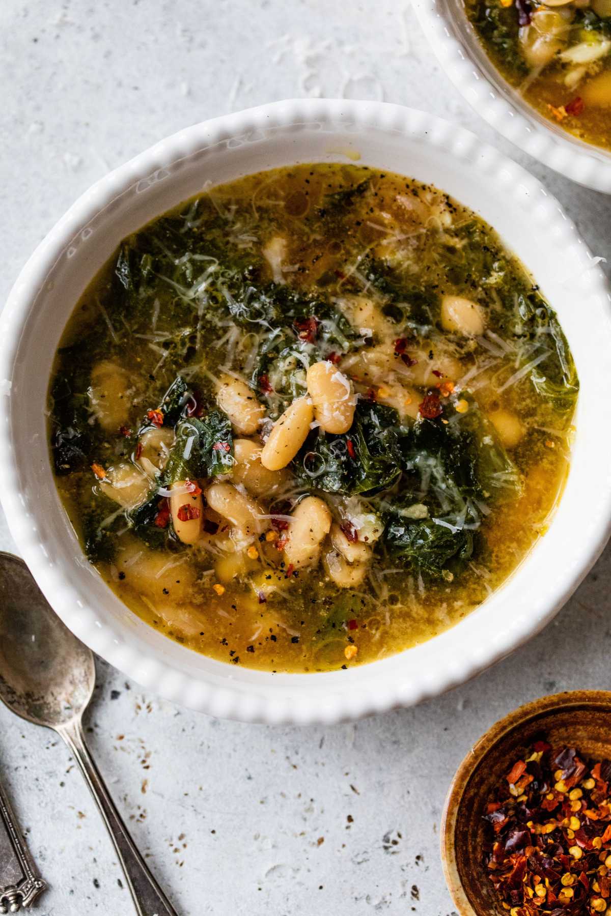White bean soup with greens in a white bowl.
