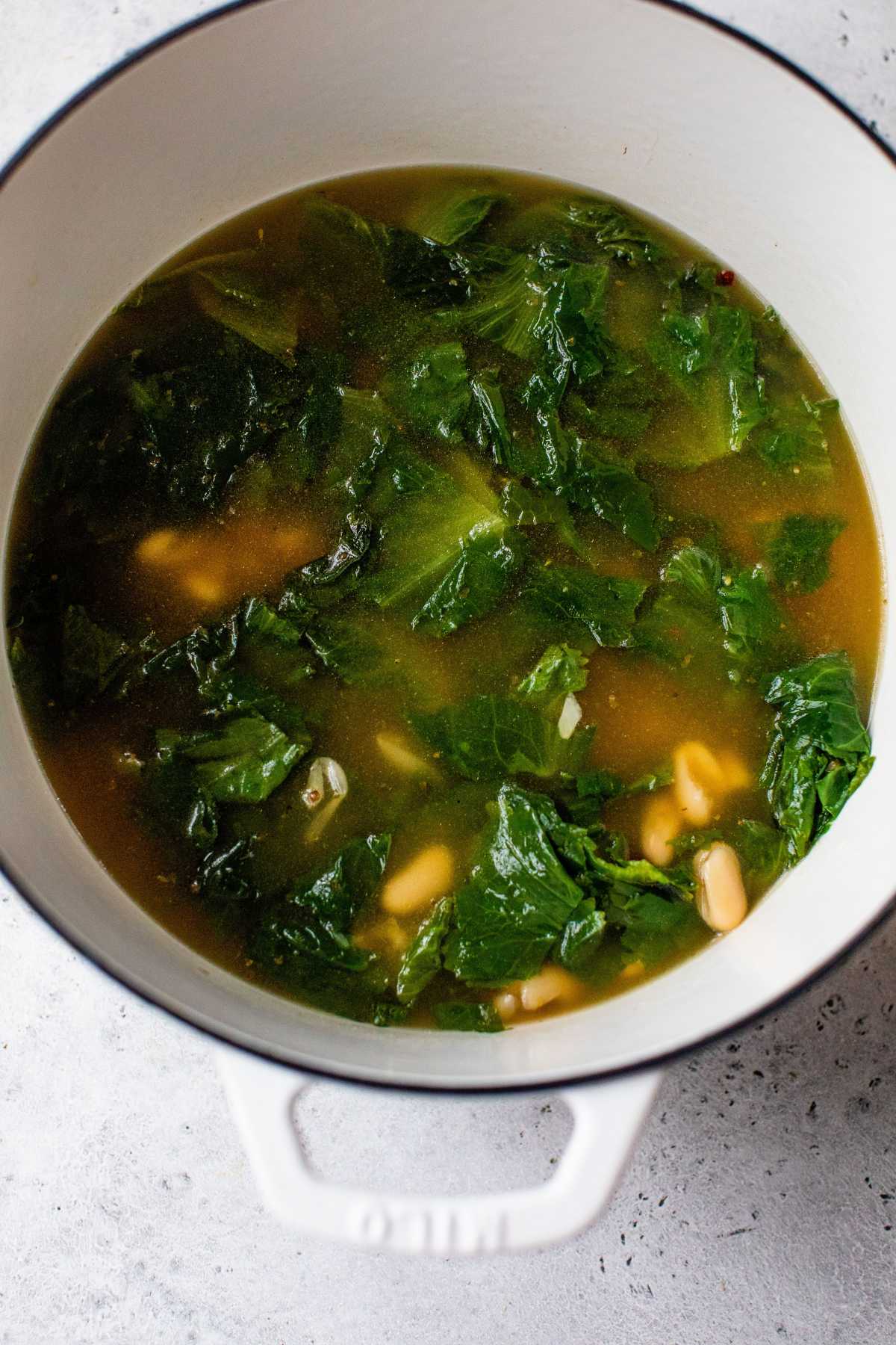 Escarole cooking with white beans in chicken broth.