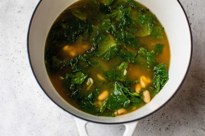 Escarole cooking with white beans in chicken broth.