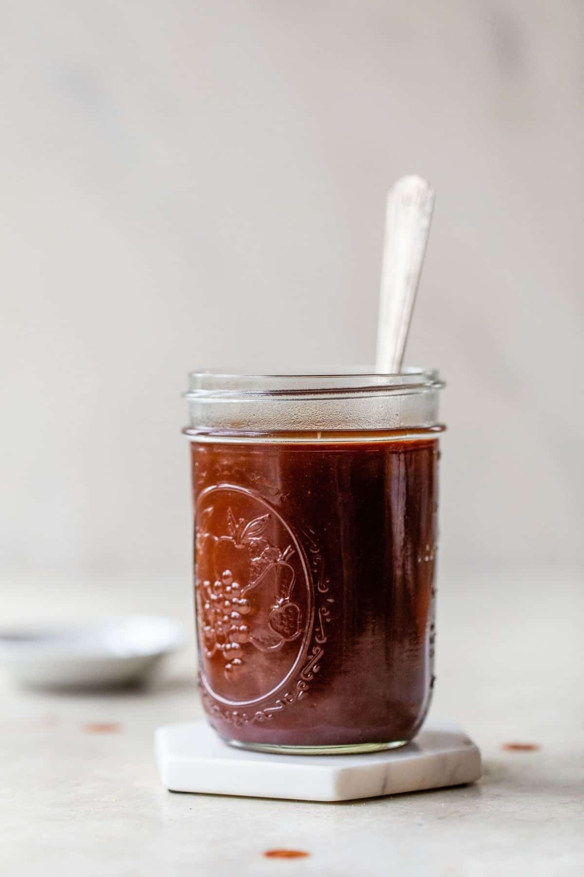 A jar of BBQ sauce with a spoon in it.