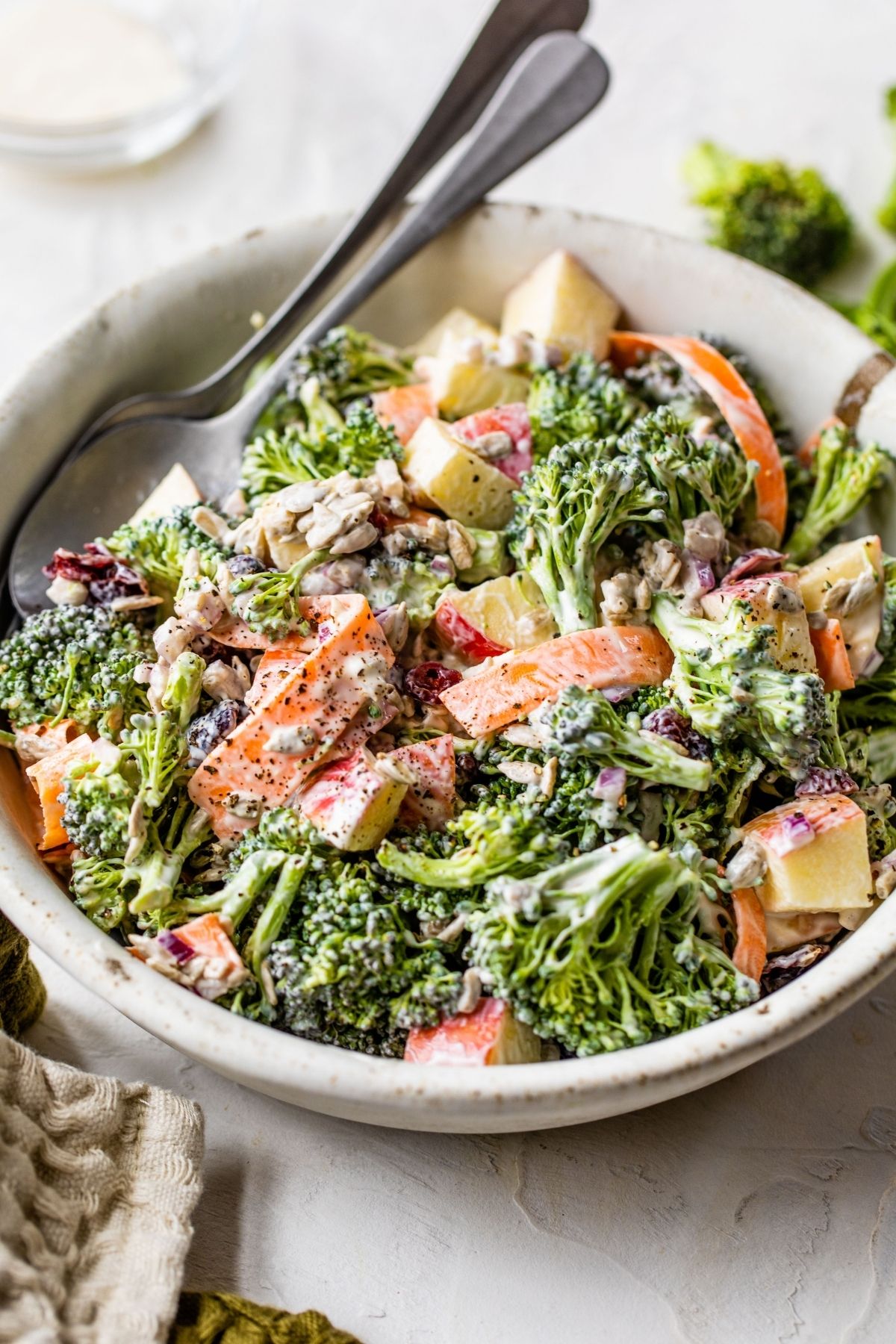 Broccoli apple salad made with shredded carrots in a white bowl.