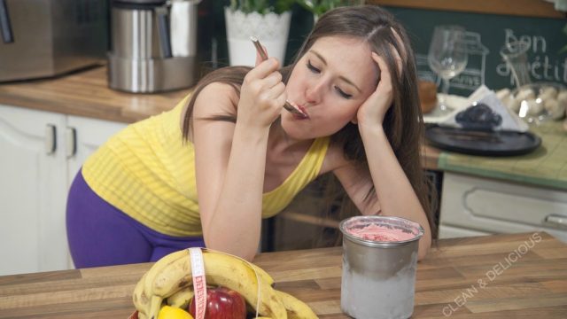 a woman is eating ice cream with her hand in her hair standing in the kitchen emotionally eating. 