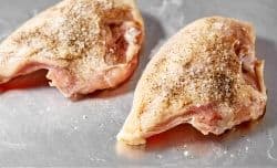 seasoned raw bone-in chicken breast on a baking pan