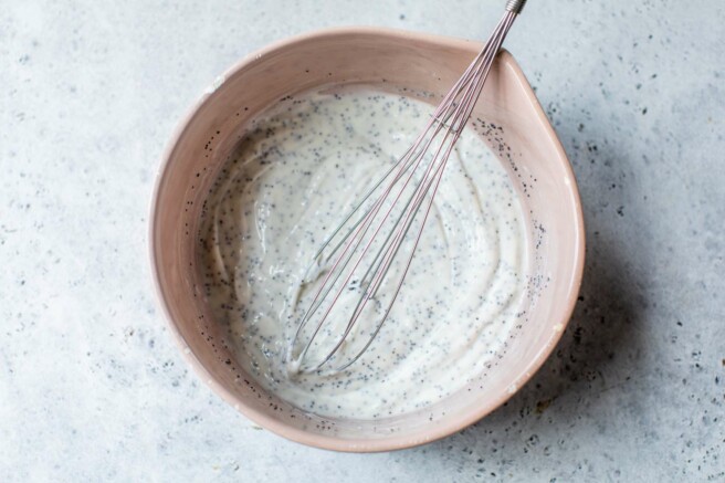 Whisking Greek yogurt with poppy seeds, honey and apple cider vinegar in a large bowl.