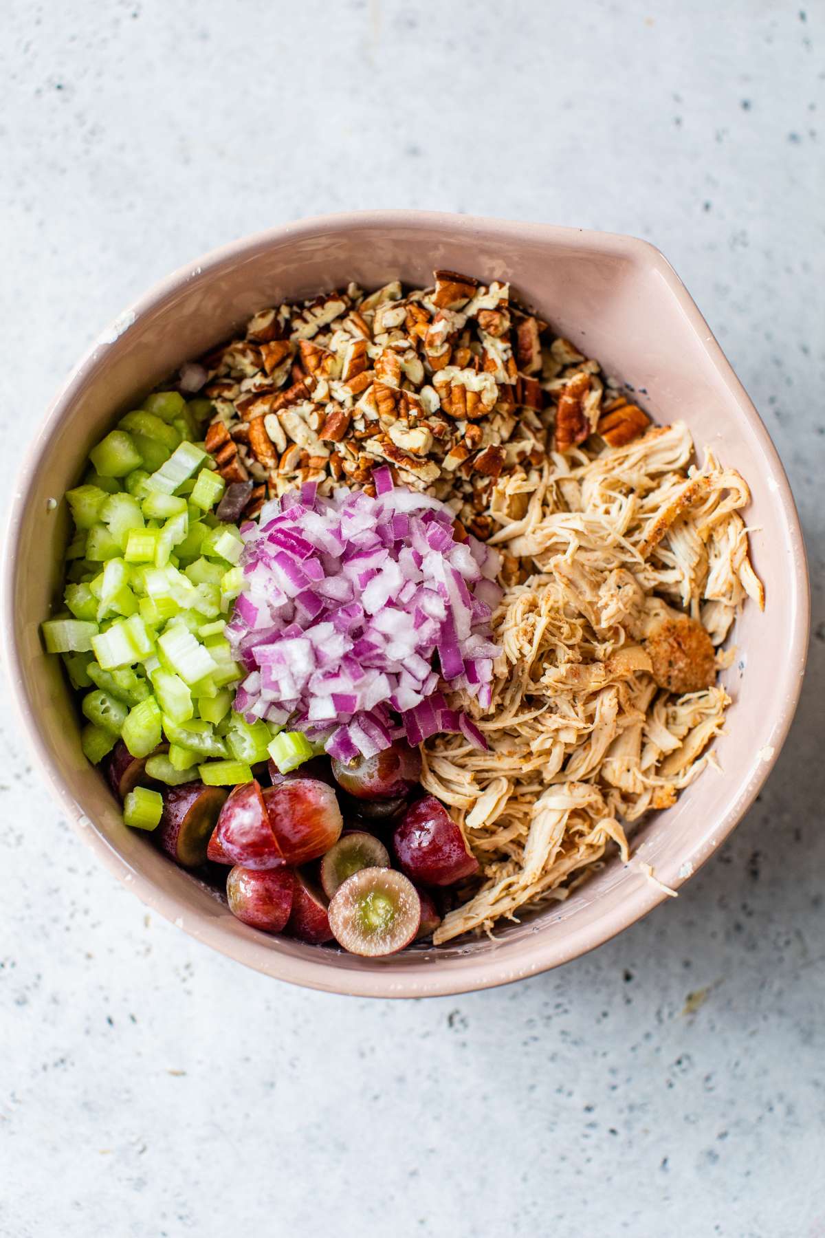 Pecans, chicken, red onion, grapes and celery in a large bowl.
