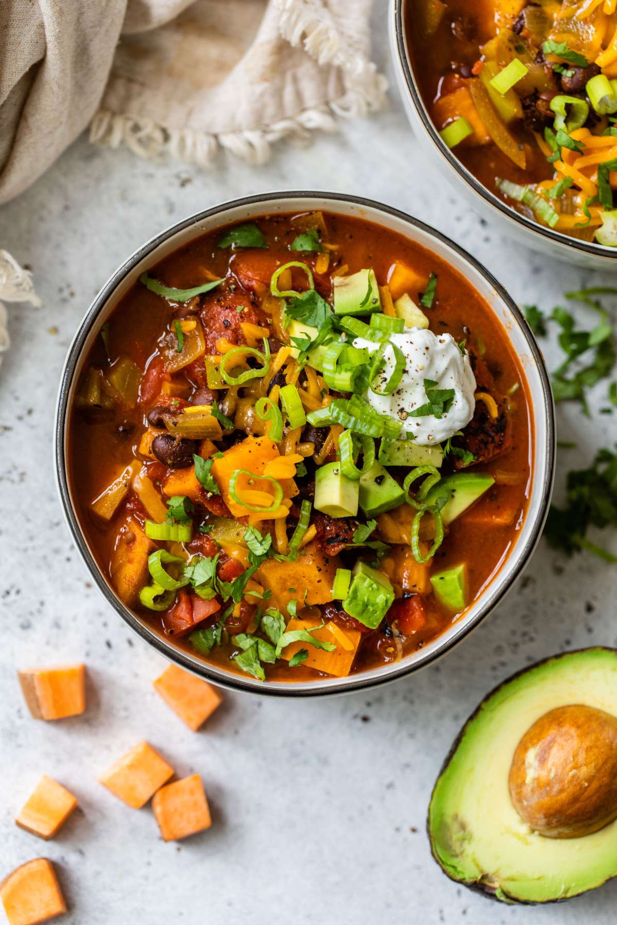 Chili with chunks of sweet potato and black beans, topped with sour cream, green onions and avocado.
