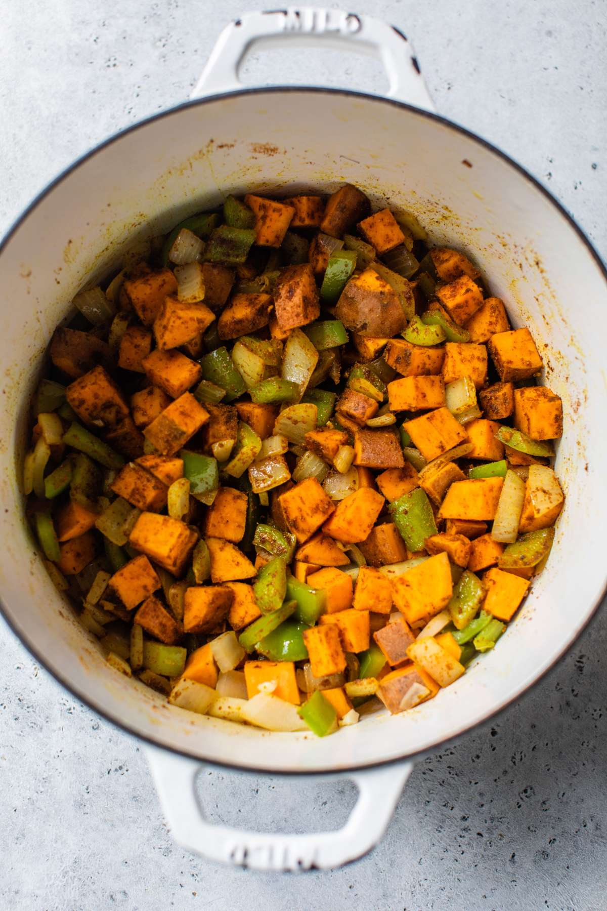 Mixing spices with chopped sweet potatoes, bell pepper and onions.