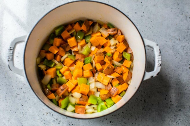 Cooking sweet potato, bell peppers and onion in a large pot.