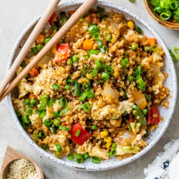 Cauliflower fried rice served in a white bowl with chopsticks.