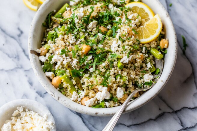 Quinoa mixed with asparagus, chickpeas, feta and fresh herbs in a white bowl.
