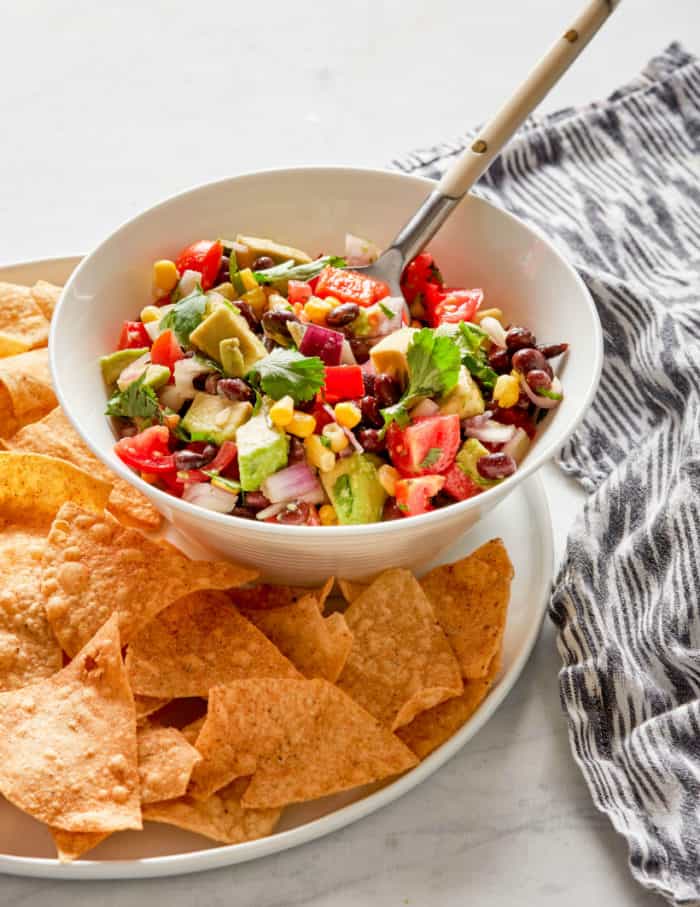 black bean salad served with tortilla chips in a white bowl with a spoon