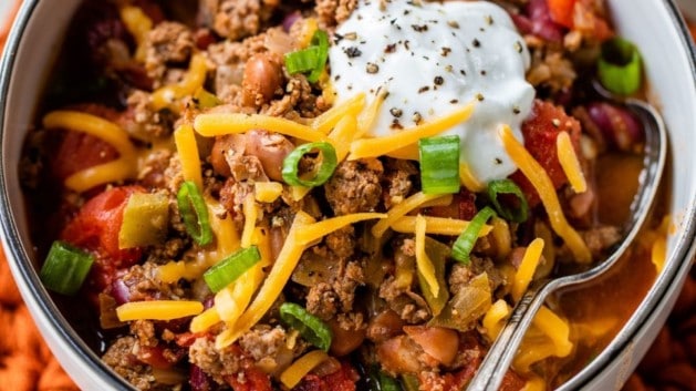 chili con carne topped with sour cream, shredded cheese and green onion