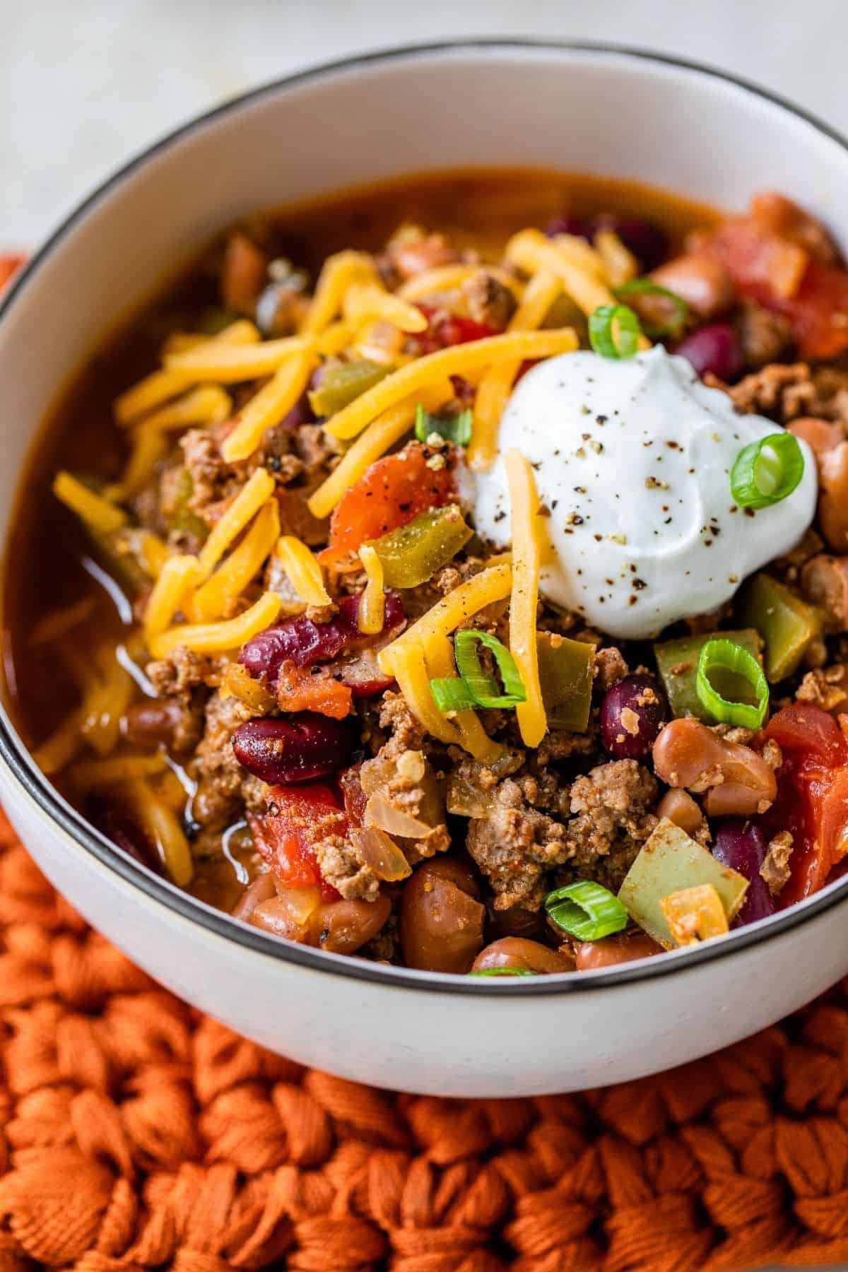 chili con carne in a white bowl and topped with sour cream and grated cheese