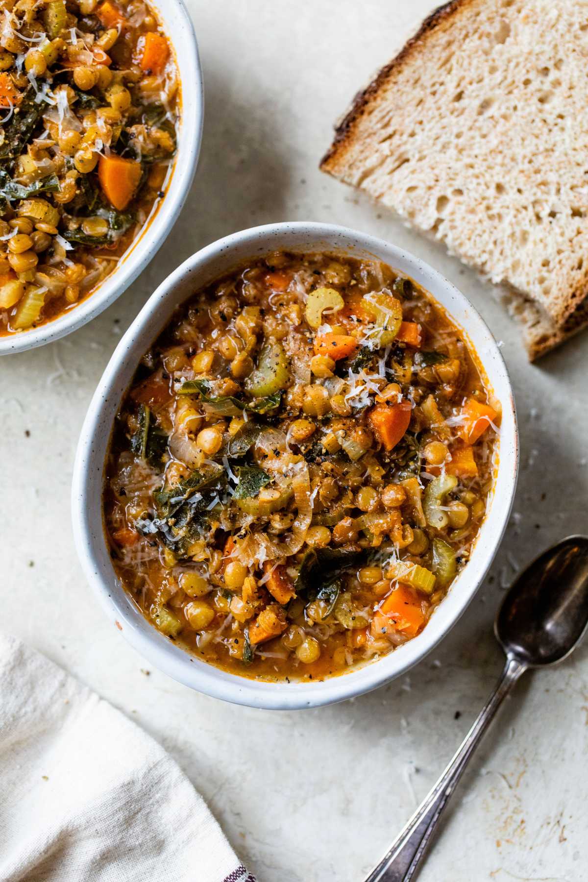Green lentil soup served in a white bowl with a slice of bread.