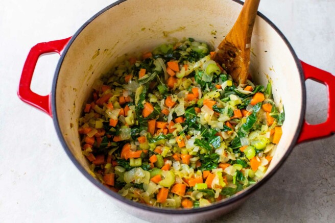 Carrots sautéing with onions and leeks in a large pot.