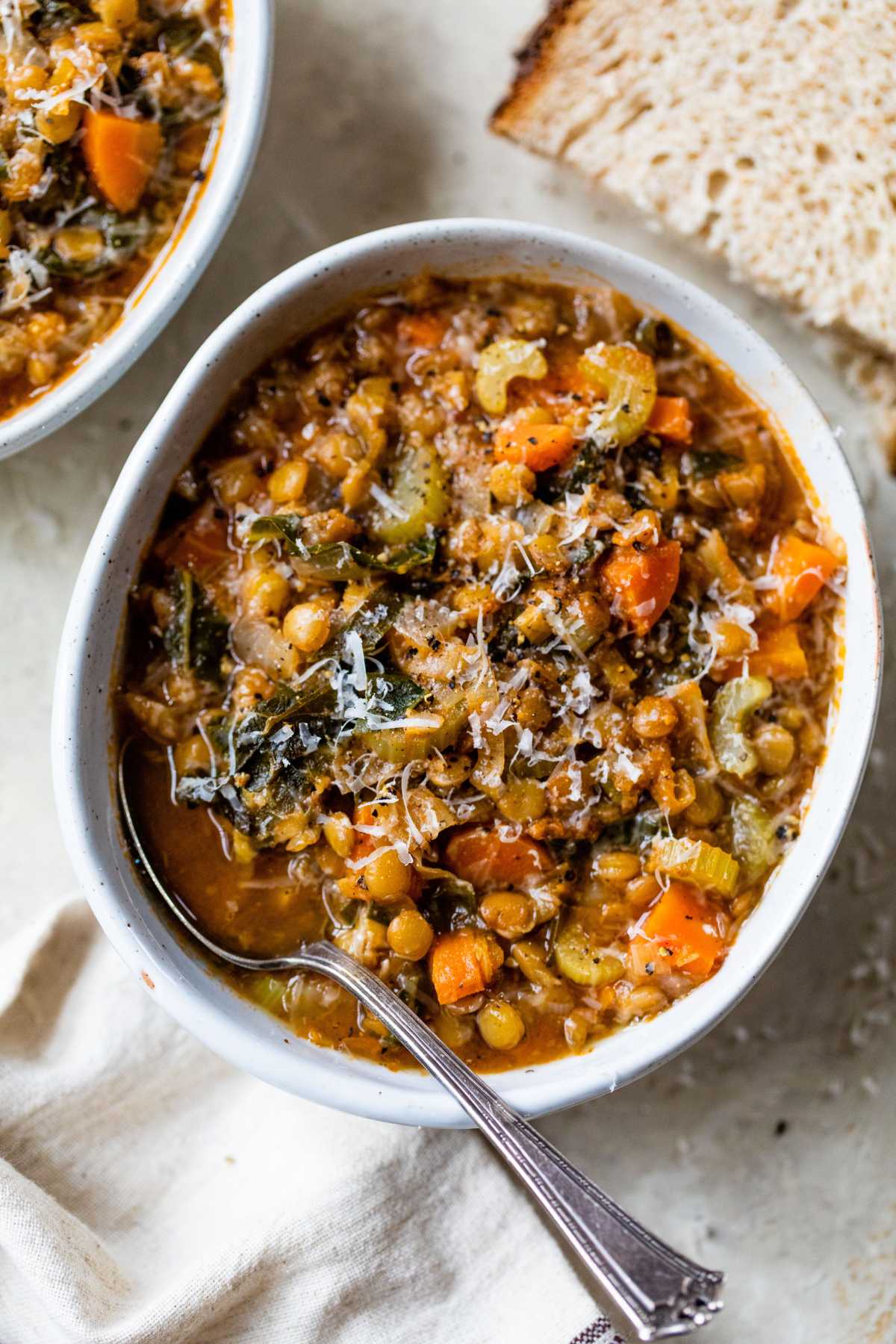 Green lentil soup made with veggies in a white bowl with a spoon.
