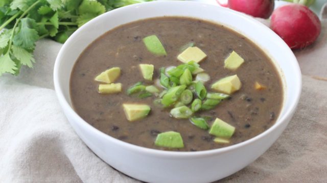 black bean soup in a white bowl topped with avocado and scallions