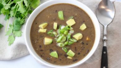 black bean soup in white bowl topped with scallions and avocados