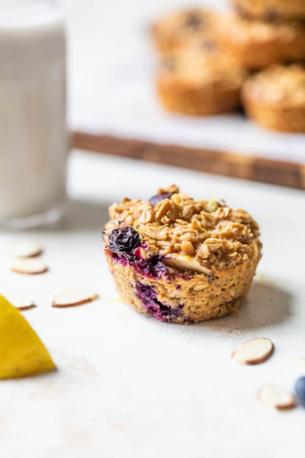 blueberry oatmeal muffin cup near a lemon slice, sliced almonds and a glass of milk