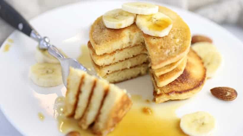 stack of fluffy almond flour pancakes topped with bananas and maple syrup on a white plate
