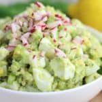 avocado egg salad in a white bowl topped with diced radishes and celery